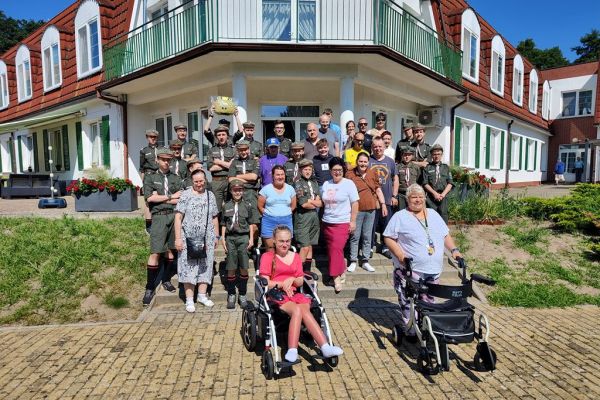 Grupowe zdjęcie mieszkańców z harcerzami na schodach zewnętrznych.