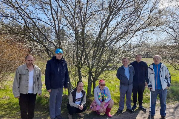 Grupa Mieszkańców pozuje przy kwitnącym drzewie śliwkowym w polu.