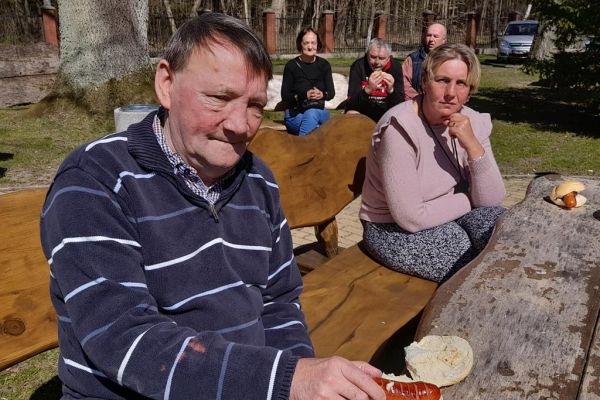 Mieszkańcy odpoczywają na ławkach przy domu pomocy i jedzą kiełbaskę z grilla.