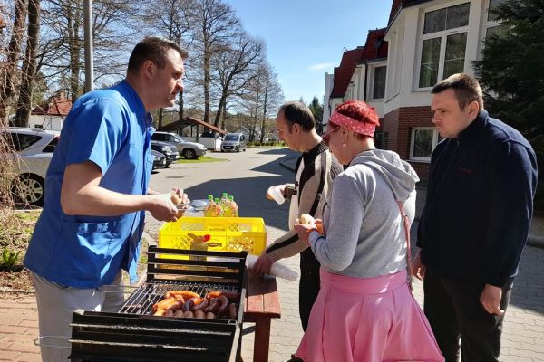 Miedzkańcy podchodzą po kiełbaskę przy grillu.