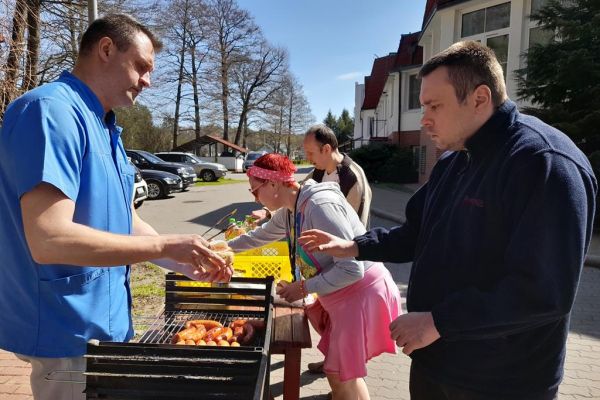 Miedzkańcy podchodzą po kiełbaskę przy grillu.
