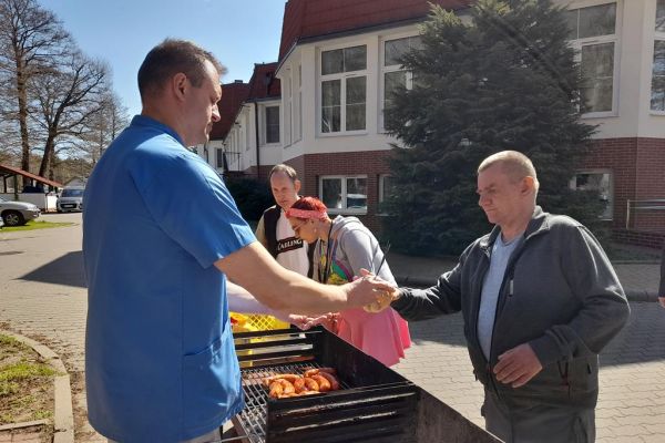 Miedzkańcy podchodzą po kiełbaskę przy grillu.