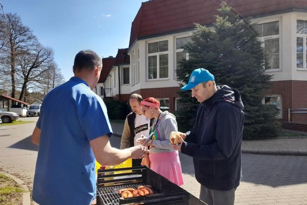 Miedzkańcy podchodzą po kiełbaskę przy grillu.