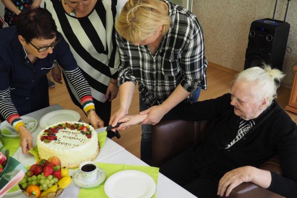 Mieszkanka wraz z pracownikami kroi torta.
