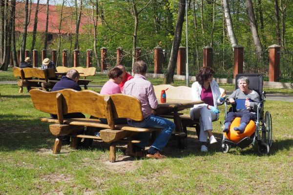 Mieszkańcy na ławeczce spożywają kiełbaskę z grilla.