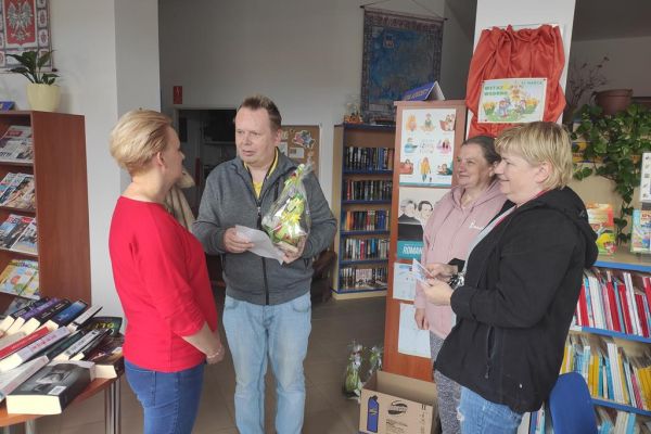 Mieszkańcy wręczają prezent z okazji Dnia bibliotekarza pani z biblioteki.