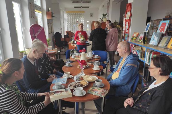Mieszkańcy na spotkaniu DKK czekają na rozpoczęcie siedząc przy stolikach.