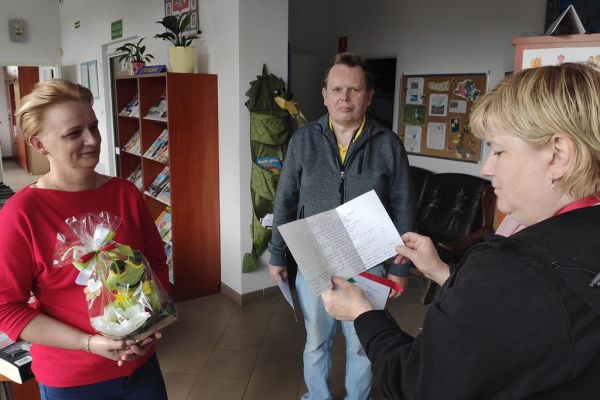 Terapetka zajęciowa czyta wiersz z okazji Dnia bibliotekarza dla pani z biblioteki.