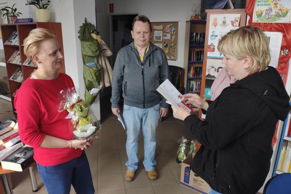 Terapetka zajęciowa czyta wiersz z okazji Dnia bibliotekarza dla pani z biblioteki.