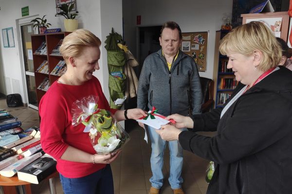 Terapetka wręcza kartkę z okazji Dnia bibliotekarza dla pani z biblioteki.