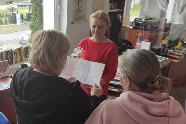 Terapetka zajęciowa czyta wiersz z okazji Dnia bibliotekarza dla pani z biblioteki.