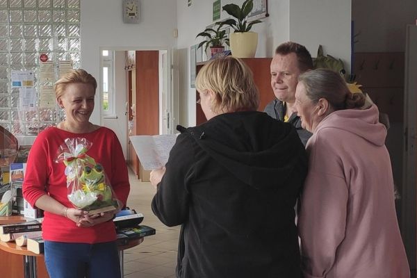 Terapetka zajęciowa czyta wiersz z okazji Dnia bibliotekarza dla pani z biblioteki.