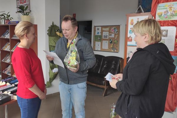 Mieszkaniec czyta życzenia z okazji Dnia bibliotekarza pani z biblioteki.