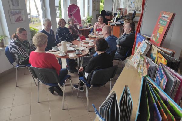 Mieszkańcy naprzemiennie opowiadają o przeczytanych książkach oraz słuchają wypowiedzi pani bibliotekarki siedząc przy stolikach.