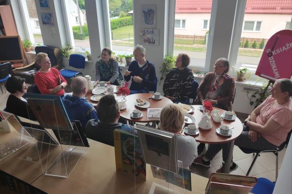 Mieszkańcy naprzemiennie opowiadają o przeczytanych książkach oraz słuchają wypowiedzi pani bibliotekarki siedząc przy stolikach.