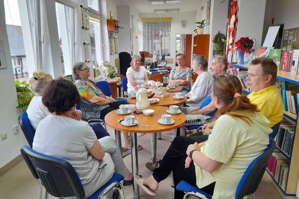 Grupa uczestników DKK siedzących przy stolikach z poczęstunkiem.