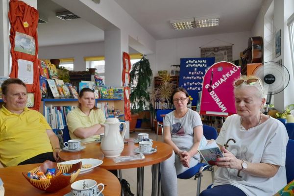 Mieszkanka domu czyta wiersze a pozostali uczestnicy słuchają.