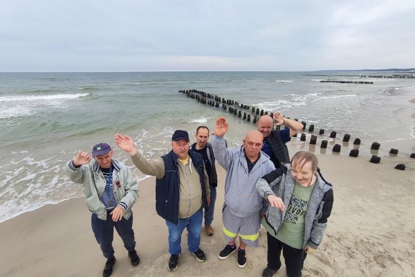 Mieszkańcy machają do zdjęcia grupowego na tle morza na plaży w Ustce.