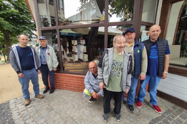 Mieszkańcy stoją przy witrynie restauracji w której widać model żaglowca.