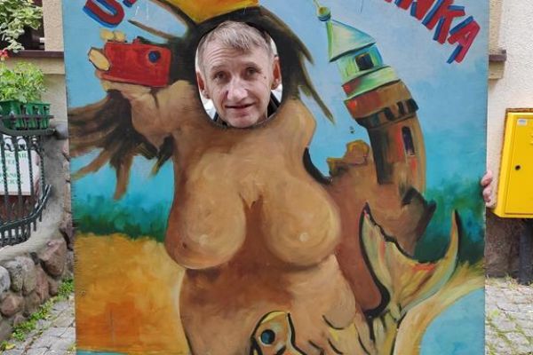 Mieszkaniec pozuje do zdjęcia z włożoną głową w makietę do zdjęć przedstawiająca humorystyczną Syrenkę ustecką.ć 