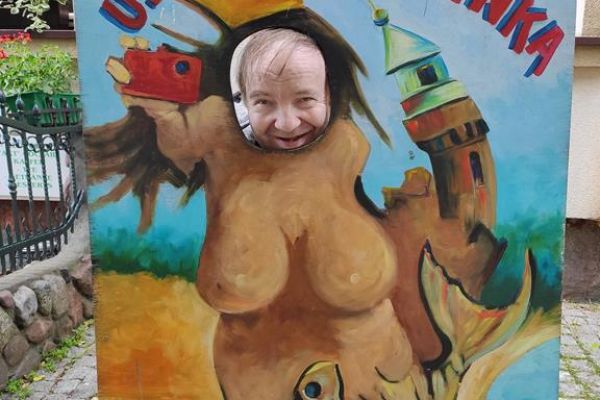 Mieszkaniec pozuje do zdjęcia z włożoną głową w makietę do zdjęć przedstawiająca humorystyczną Syrenkę ustecką.
