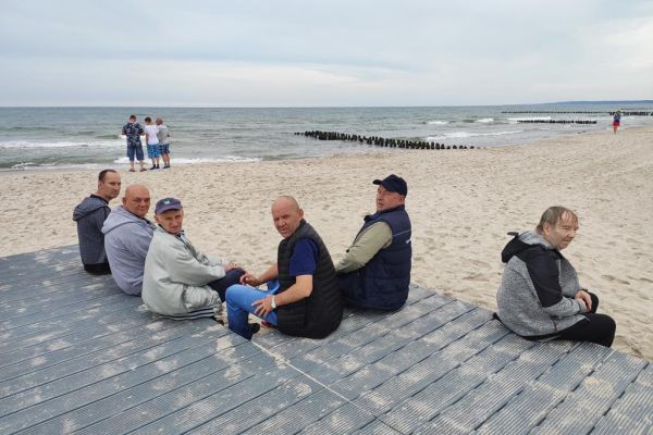 Mieszkańcy siedzą na drewnianym trakcie prowadzącym na plażę w Ustce na tle morza.