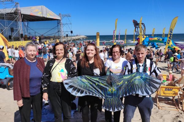 Mieszkańcy pozują do zdjęcia na plaży w Ustce z latawcem w kształcie orła.
