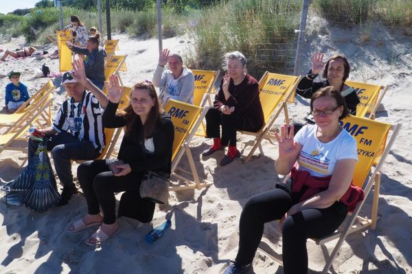 Mieszkańcy siedzą na leżakach RMF fm na plaży w Ustce.