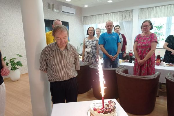 Mieszkańcy i jubilat stoją wpatrując się w fontannę na torcie.