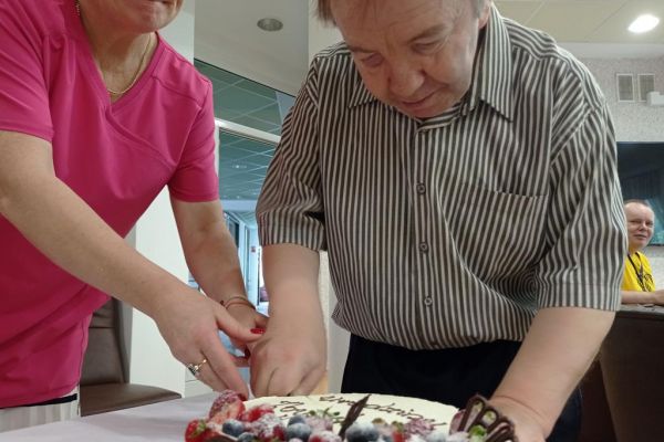 Mieszkaniec Pan Zbyszek kroi tort z opiekunem.