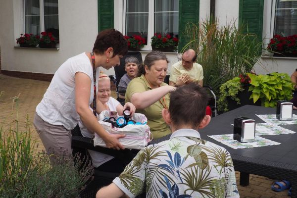 Mieszkańcy częstują się rozdawanymi lodami i je spożywają w upalny dzień siedząc na tarasie Domu.