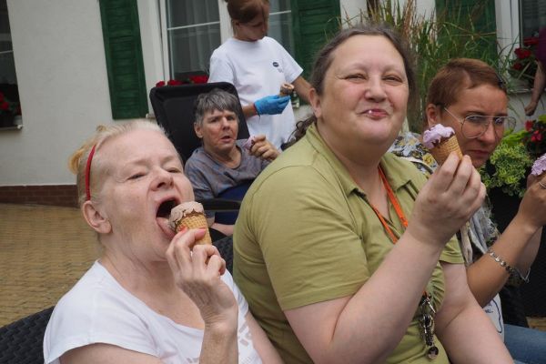 Mieszkańcy częstują się rozdawanymi lodami i je spożywają w upalny dzień siedząc na tarasie Domu.