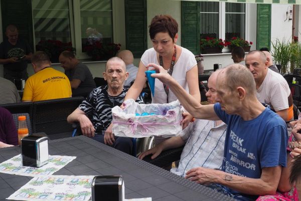 Mieszkańcy częstują się rozdawanymi lodami i je spożywają w upalny dzień siedząc na tarasie Domu.