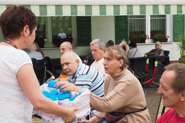 Mieszkańcy częstują się rozdawanymi lodami i je spożywają w upalny dzień siedząc na tarasie Domu.