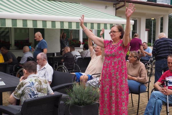 Mieszkańcy częstują się rozdawanymi lodami i je spożywają w upalny dzień siedząc na tarasie Domu.
