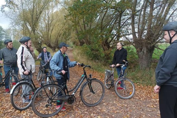 Mieszkańcy trzymając rowery słuchają na trasie wycieczki opowieści terapeuty.