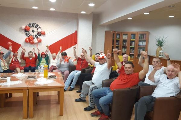 Mieszkańcy w strojach barwy biało - czerwonej oglądają mecz w kawiarence i kibicują.