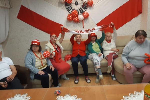 Mieszkańcy w strojach barwy biało - czerwonej oglądają mecz w kawiarence i kibicują.