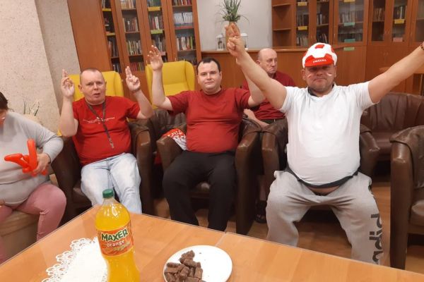 Mieszkańcy w strojach barwy biało - czerwonej oglądają mecz w kawiarence i kibicują.