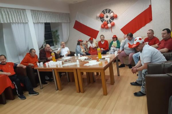 Mieszkańcy w strojach barwy biało - czerwonej oglądają mecz w kawiarence i kibicują.