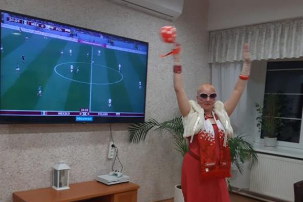 Mieszkańcy w strojach barwy biało - czerwonej oglądają mecz w kawiarence i kibicują.