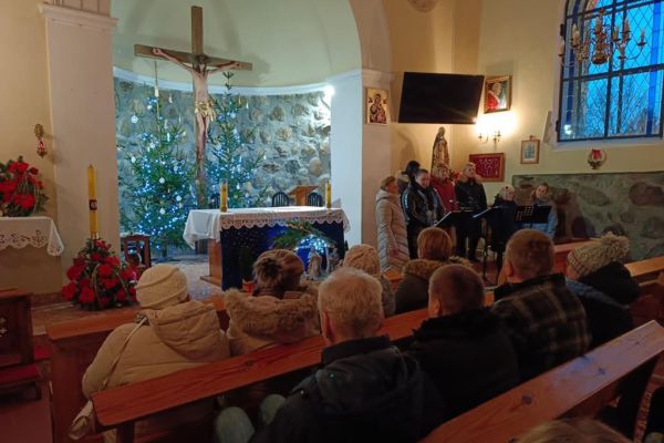 Mieszkańcy wraz z innymi uczestnikami koncertu słuchaja kolęd siedząc w ławce w kościele w Rowach.