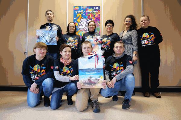 Mieszkańcy  i pracownicy w koszulkach WOŚP trzymaja obrazy na aukcję.