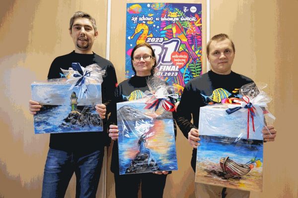 Mieszkańcy w koszulkach WOŚP trzymaja obrazy na aukcję.