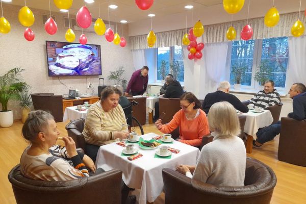 Mieszkańcy przy stolikach z poczęstunkiem i muzyce obchodzą Dzień Babci i Dziadka.