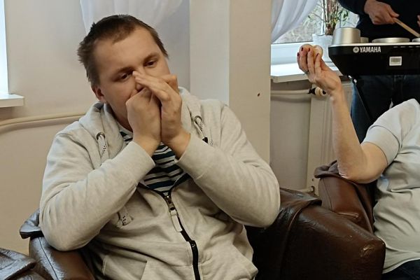 Mieszkańcy ćwiczą i wystukują rytmy na róznych instrumwentach siedząc w fotelikach przy stole wyłożonym instrumentami.