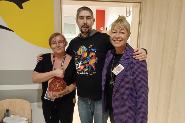 Mieszkaniec w koszulce WOŚP z dwoma Paniami wolontariuszkami gdy przekazuje pieniążki do puszki.