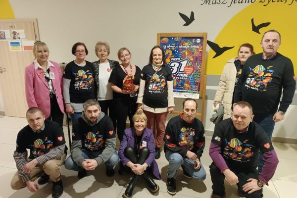 Zdjęcie grupowe mieszkańców w koszulkach WOŚP z dwoma Paniami wolontariuszkami gdy przekazują pieniążki do puszki.