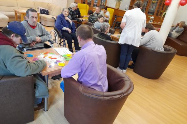 Mieszkańcy układają gry logiczne i myślowe przy stolikach.