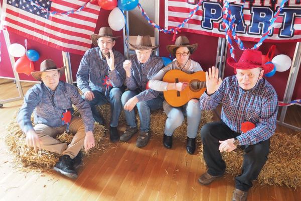 Mieszkańcy w kapeluszach kowbojskich siedzą na ułozonej słomie i pozują do zdjęcia.